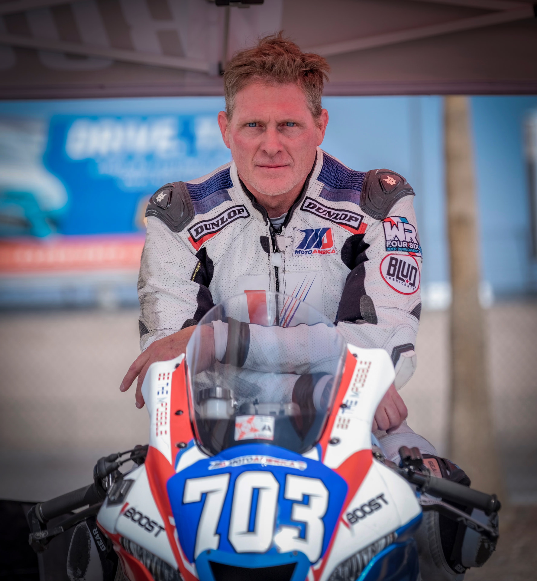 Joel Powell in his racing leathers beside his #703 motorcycle in the paddock